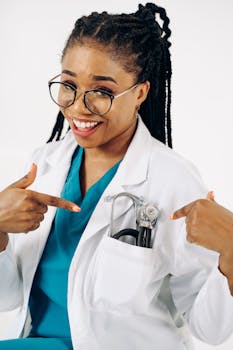Cheerful female doctor in white coat pointing at stethoscope, embodying modern healthcare professionalism.
